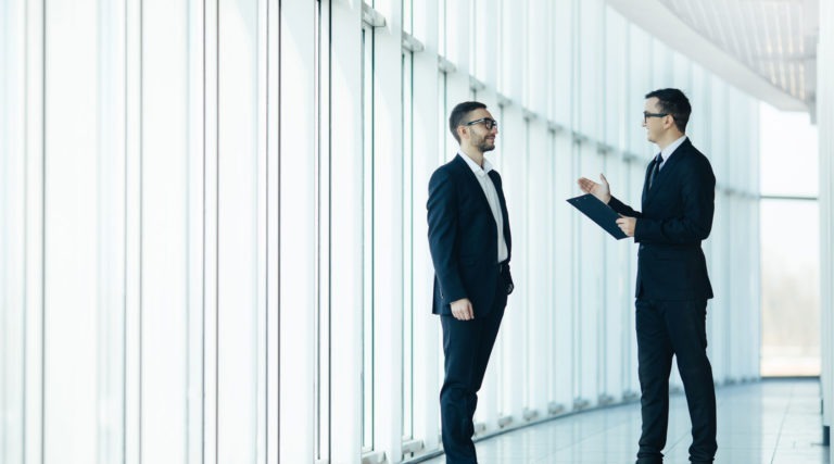 Two men in suits standing and talking to each other in a hall