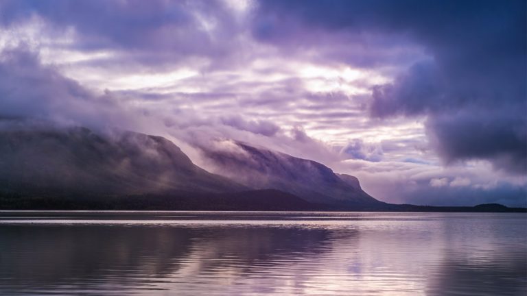 Eye level view of a body of water with mountains and a purple sky in the background