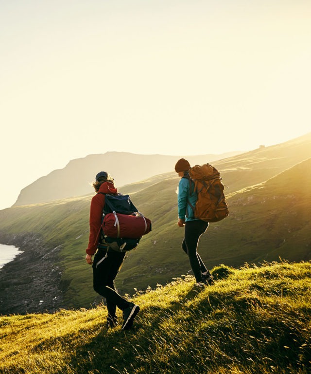 Two people with hiking gear on walking down a grassy hill