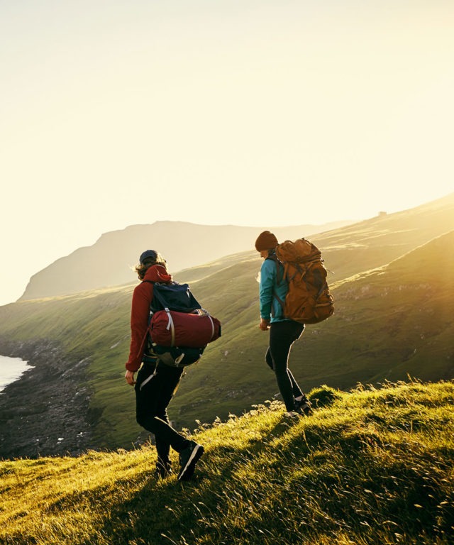 Two people with hiking gear on walking down a grassy hill