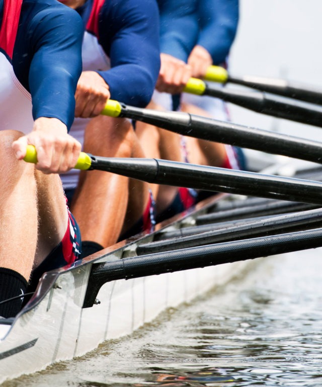 The side of a rowboat with several people rowing