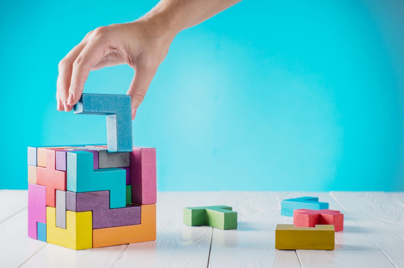 Hand putting colorful, tetris-like building blocks into cube. 