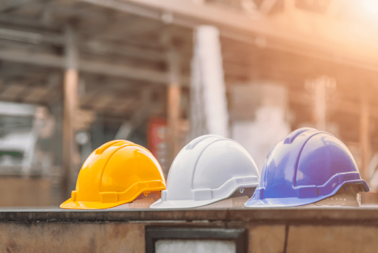 A yellow construction hat, a white construction hate, and a blue construction hat sitting on top of a metal fence in a construction zone