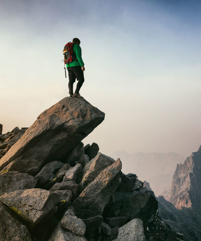 A person with hiking gear standing on a rock over looking a cliff and mountains