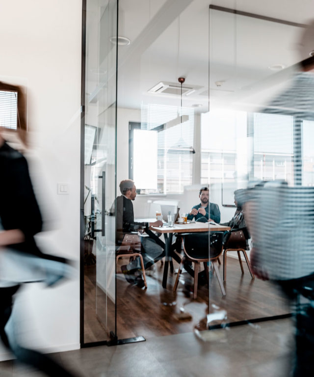 Three people talking while sitting at a table in a glass office