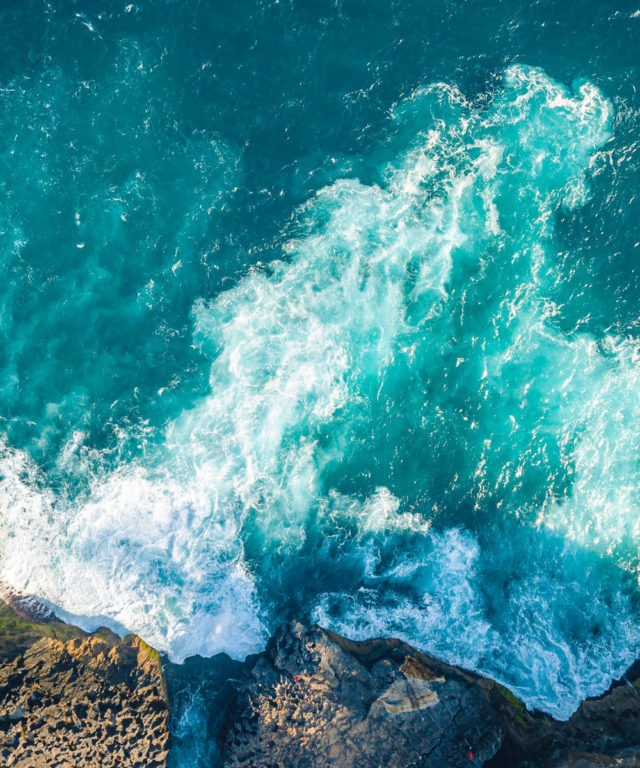 Bird's-eye view of waves crashing into the side of a cliff