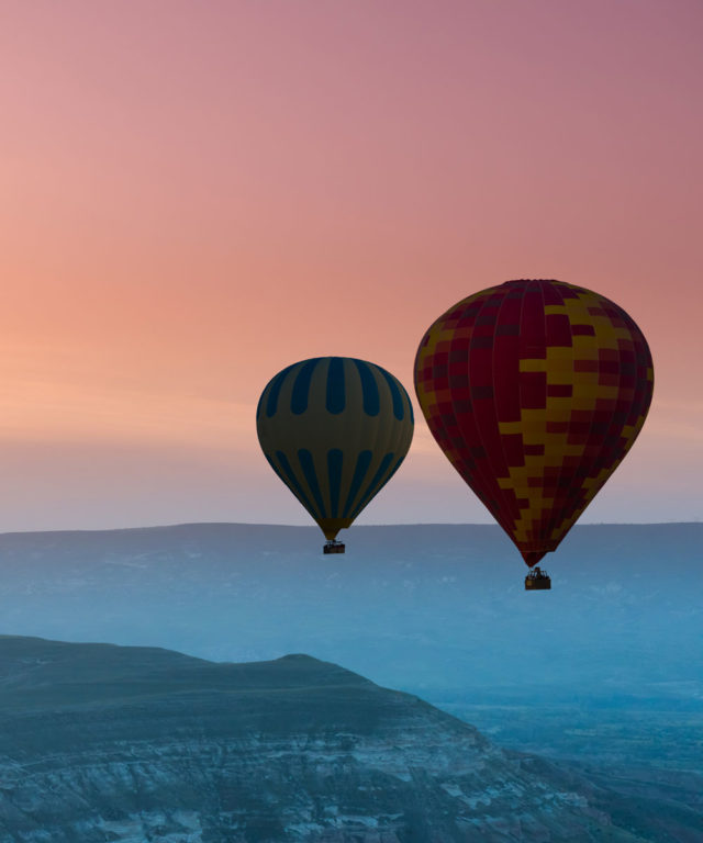 Two hot air balloons floating over mountains with a colorful sky