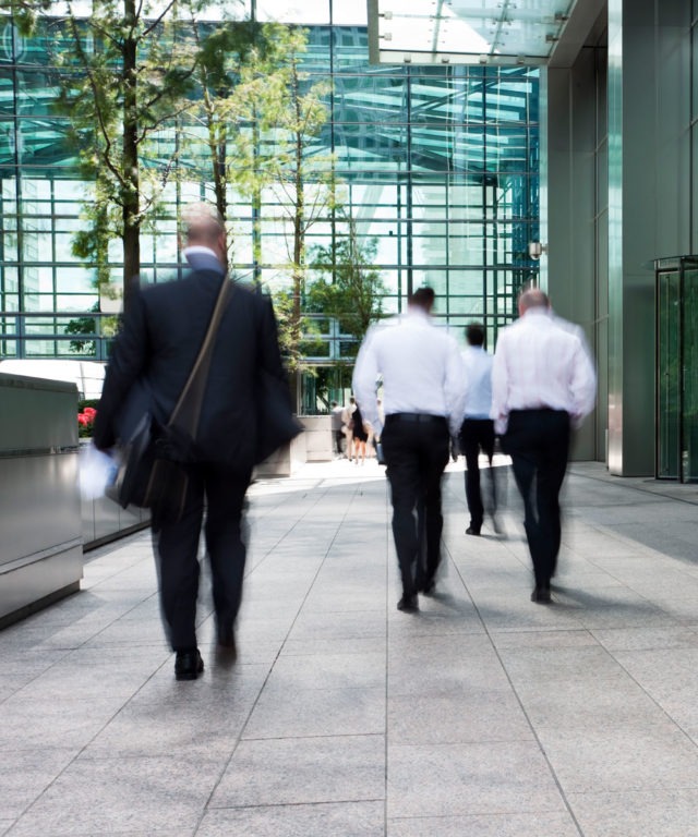 People in suits walking up to a building made of glass