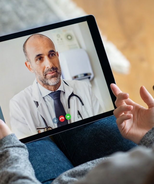 A digital tablet in a persons lap with a doctor on the screen as a video call