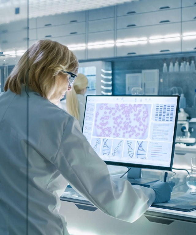 A woman working in a lab with goggles on looking at a computer screen