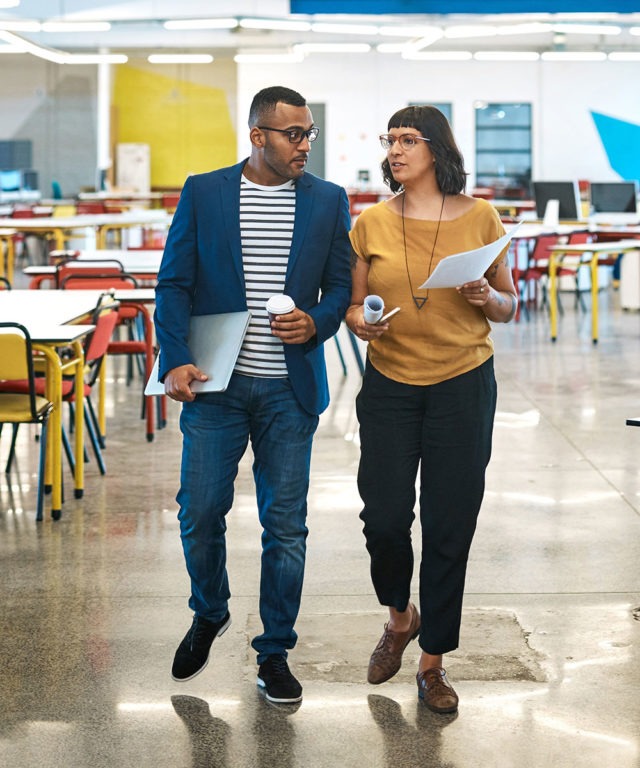 A man and a woman walking next to each other having a discussion in an office space