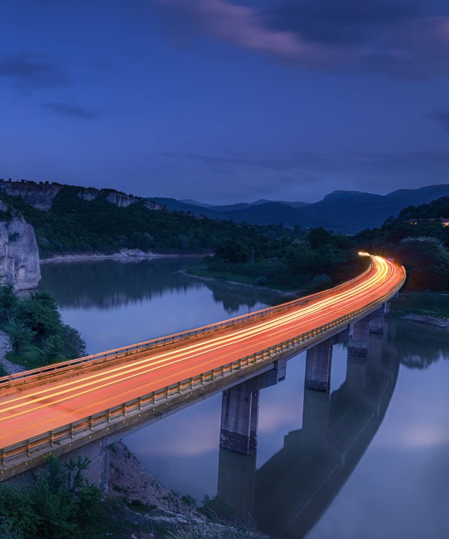 A highway at nighttime going over a river with car lights blurred over the road