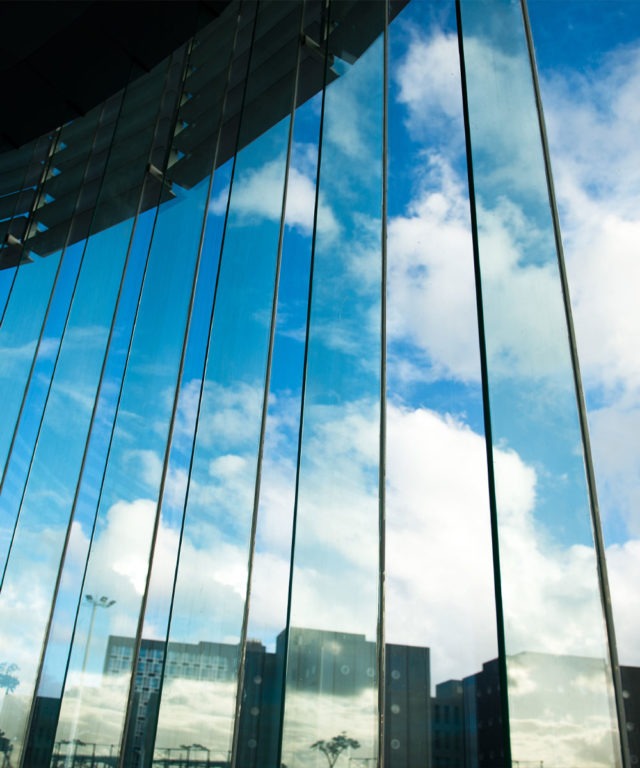 Eye-level view of large window panels inside a building with other buildings in the distance
