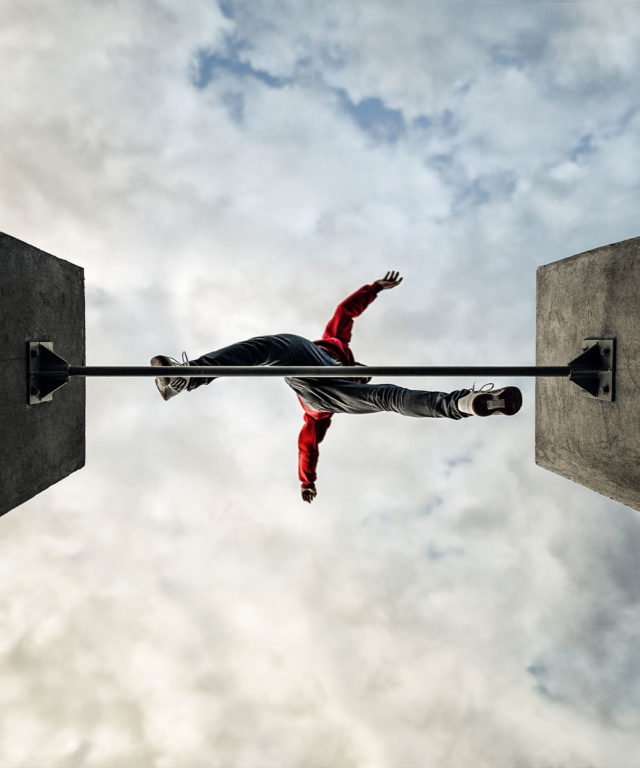 Worms-eye view of two concrete blocks connected by a metal pole and a person jumping from one block to the other