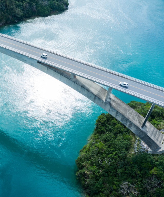 A bridge with two cars driving on it going over a large, blue body of water