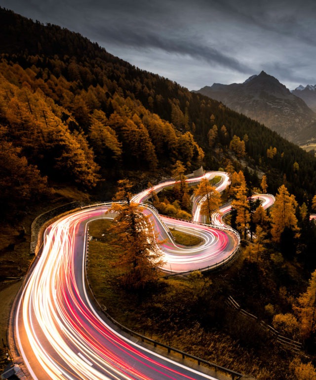 A winding road on the side of a hill with bright blurred car lights on the road