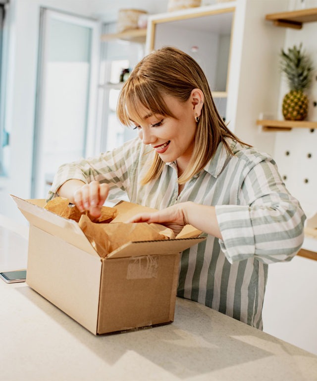 A woman standing at a counter opening a cardboard box