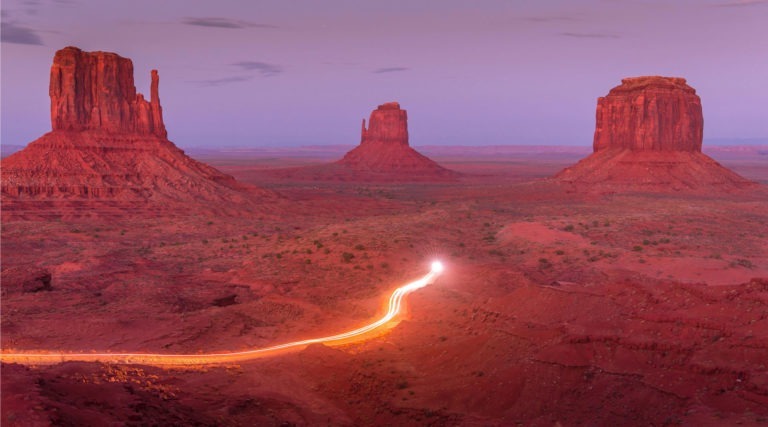 A dessert with three large rock formations and a bright blurry light traveling through the middle
