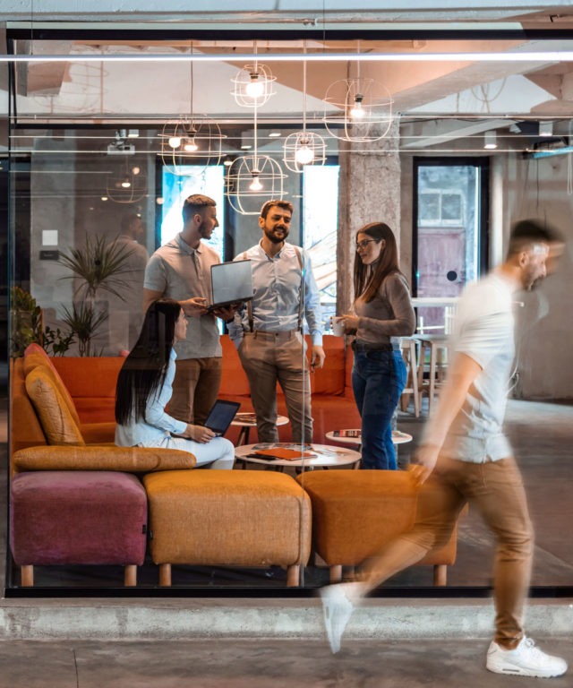 A group of people standing in a lounge area with their laptops while talking