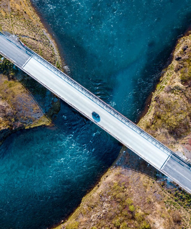 Bird's-eye view of a single car driving over water on a bridge