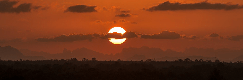 Sun setting behind clouds with orange hues