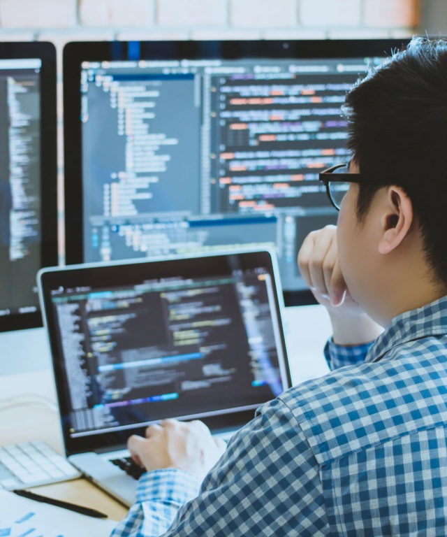 Man working on laptop in front of two desktop screens