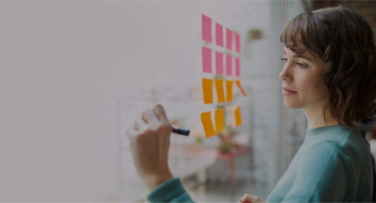 Woman writing on glass pane with sticky notes on it