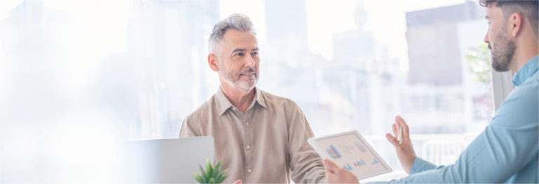 Two businessmen talking at conference table with tablets and laptop