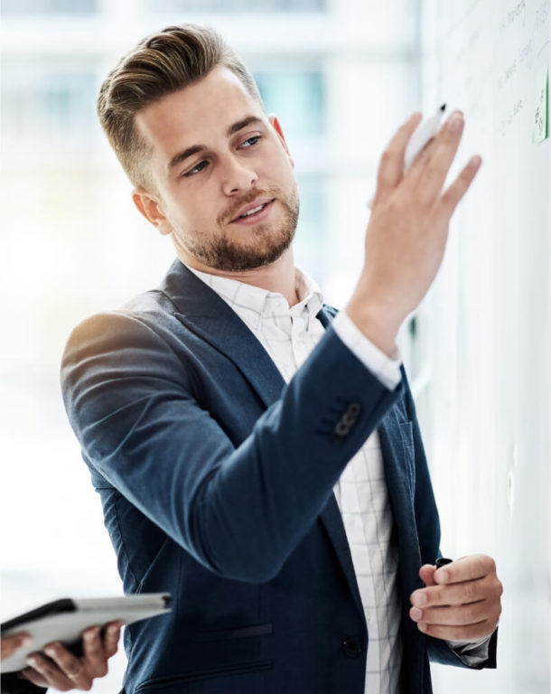 Businessman writing on whiteboard while business woman looks on