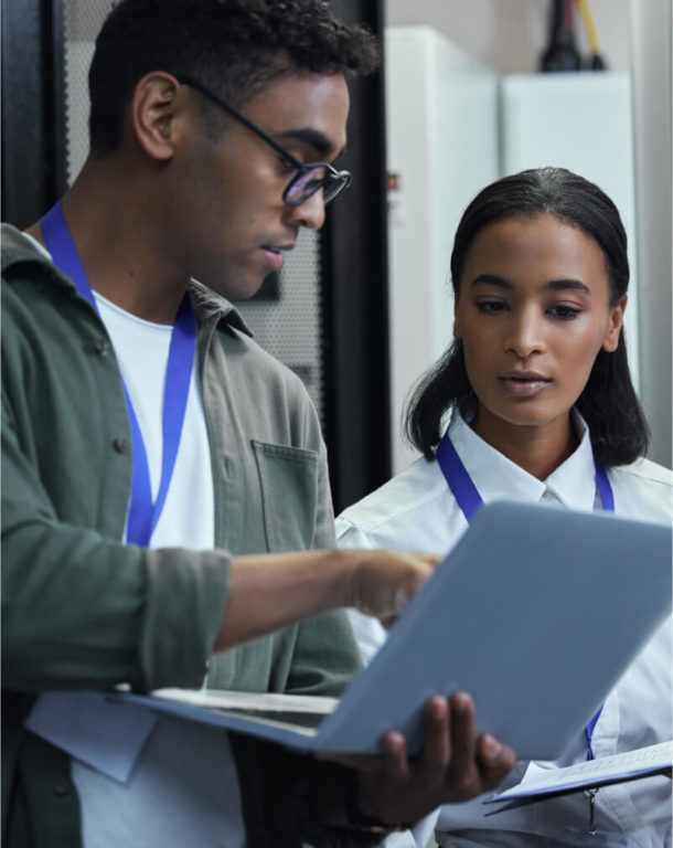 IT man pointing to laptop while woman looks on in server room