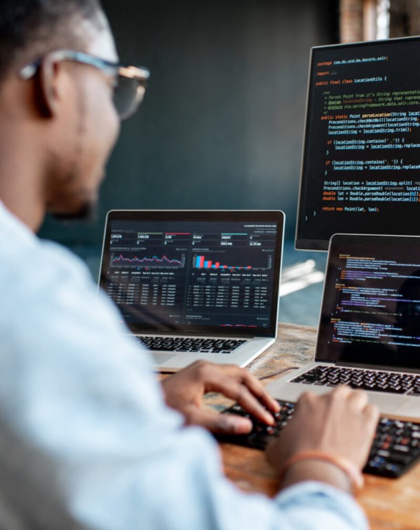 Man looking at a monitor and two laptop computers with code on it