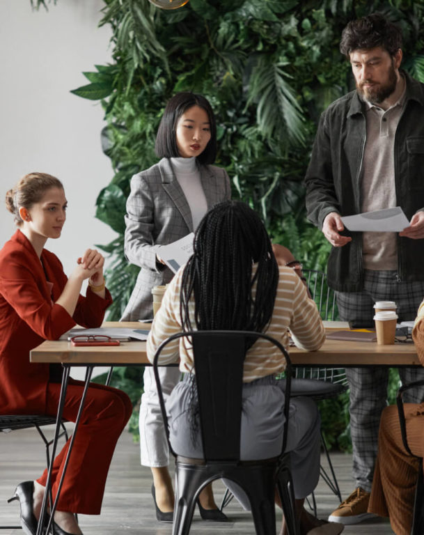 Five coworkers sitting at office table with plant wall in the background