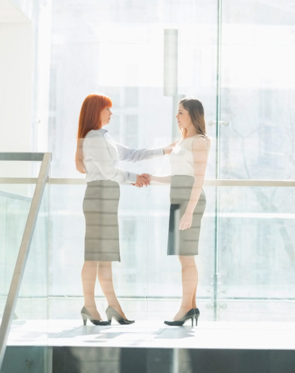 Two employees shaking hands at the top of office stairs