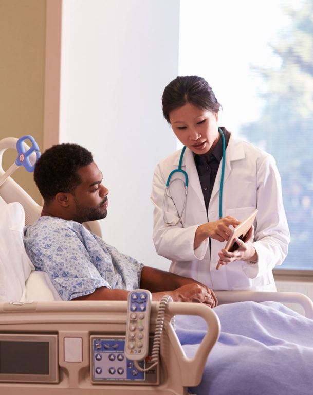 Female doctor showing tablet to male patient in hospital bed