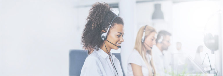 Smiling woman wearing headset typing at office computer next to coworkers