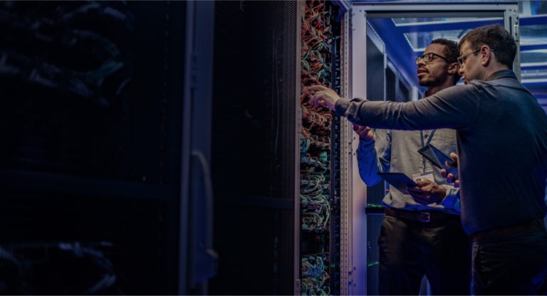 Two male IT engineers checking servers in server room with help of tablet