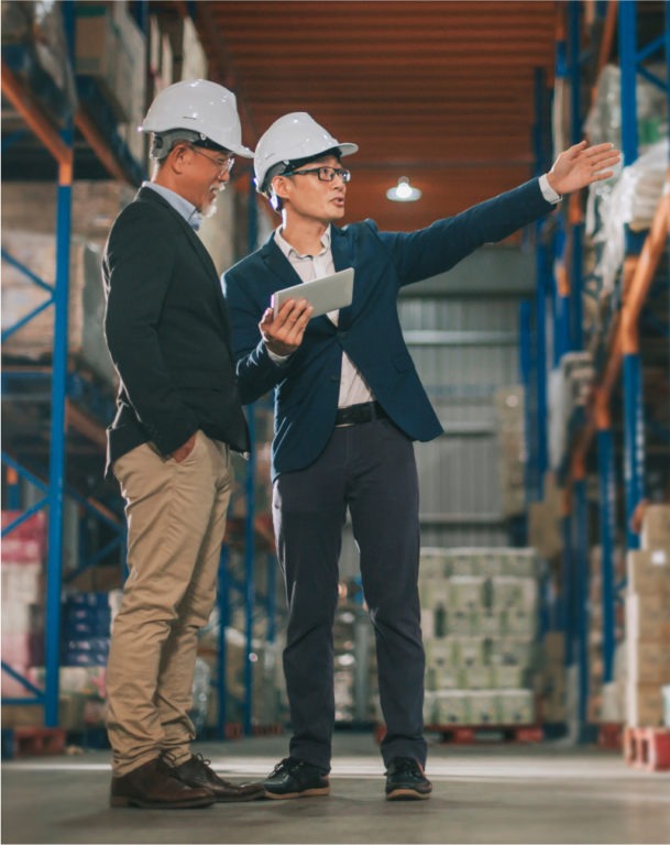 Two men wearing hardhats in warehouse, one holding digital tablet