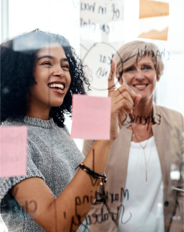 Three business women discussing notes on transparent whiteboard in office