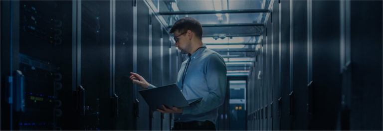 Male IT person holding laptop standing in server room