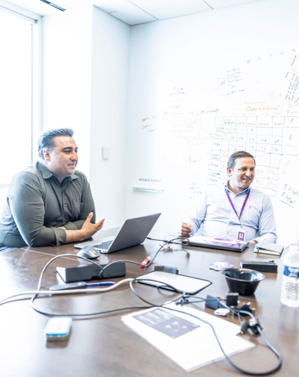 Coworkers sitting in conference room with whiteboard. 