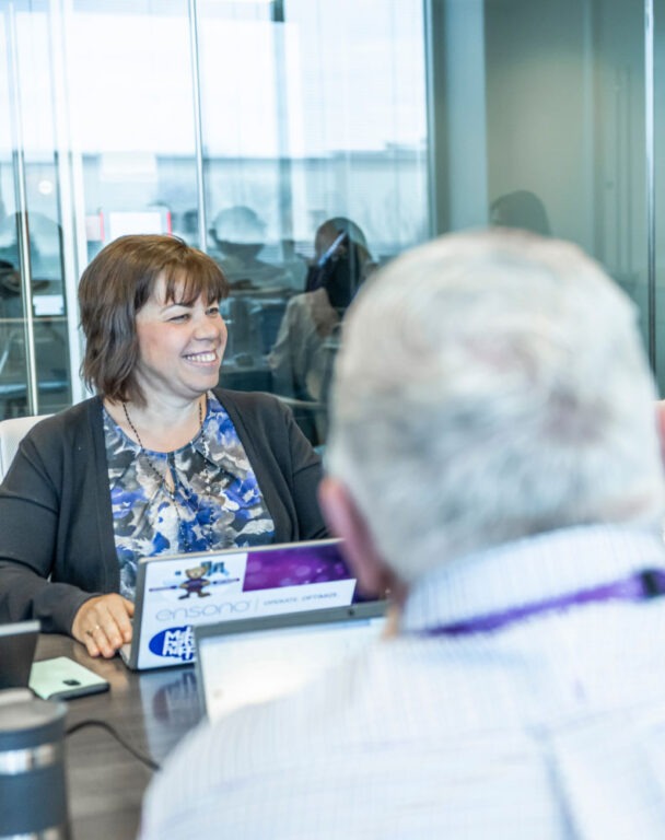 Back of workers head with woman smiling working on laptop in background