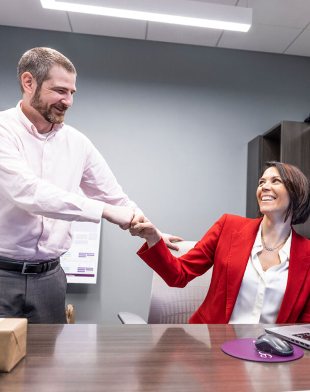 Two employees shaking hands at a desk