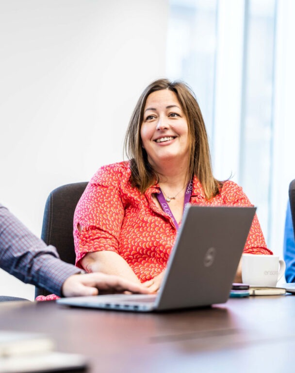 Ensono employee sitting at conference table smiling