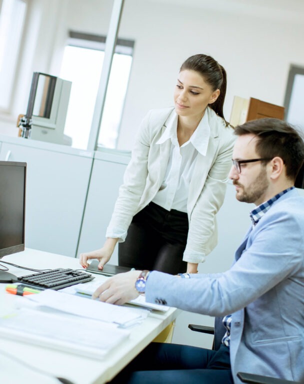 Coworker standing over employees desk and talking